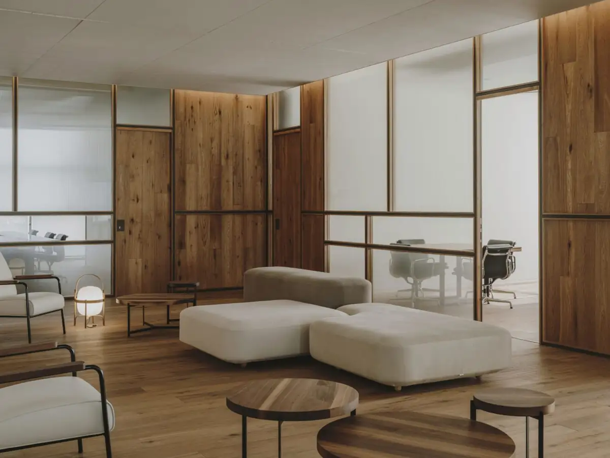 Zona de estar con sofás blancos y mesas bajas redondas de madera entre cerramientos de vidrio y madera