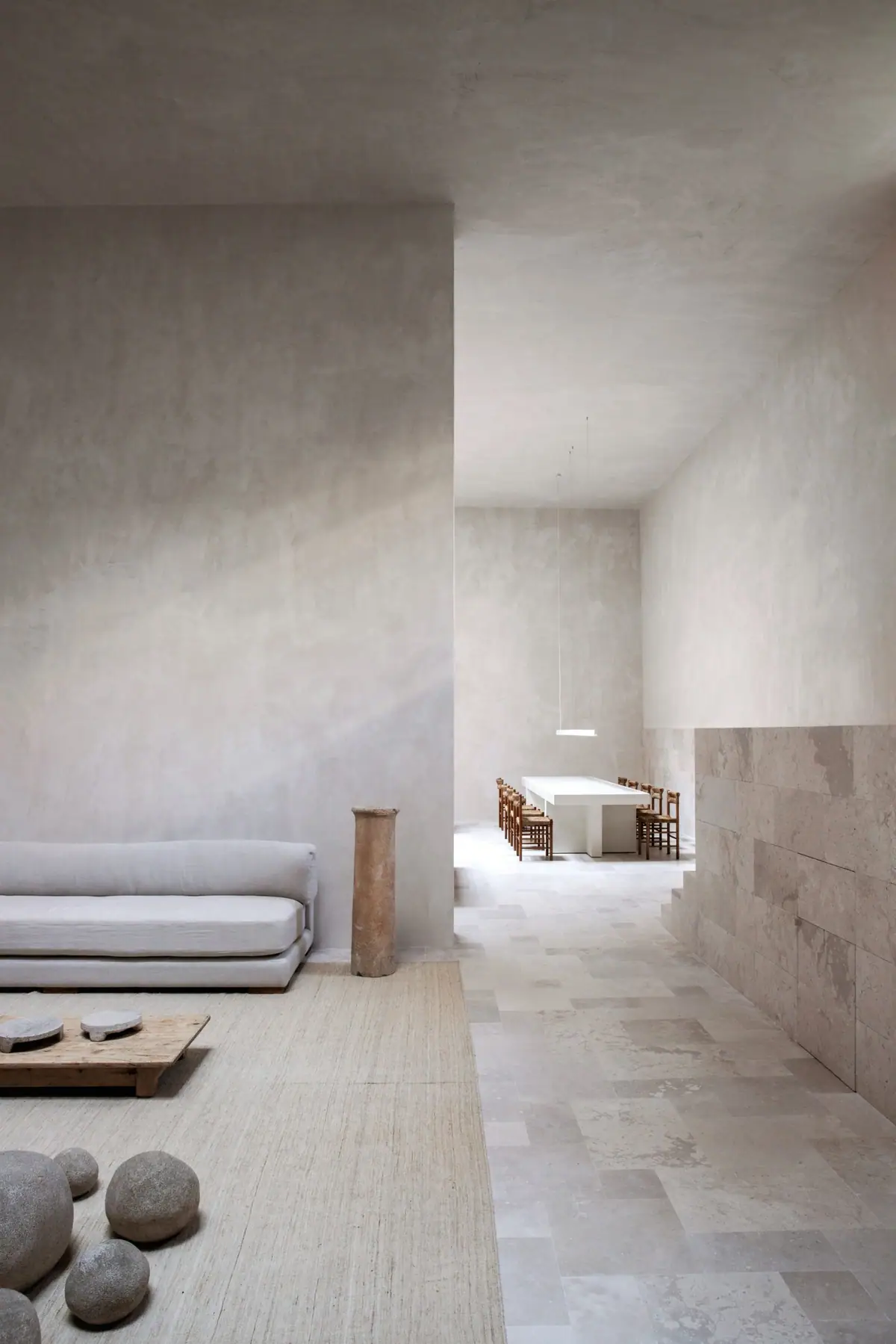 Seating area with a linen sofa and stones on a rug; in the background, the meeting table beneath the double height