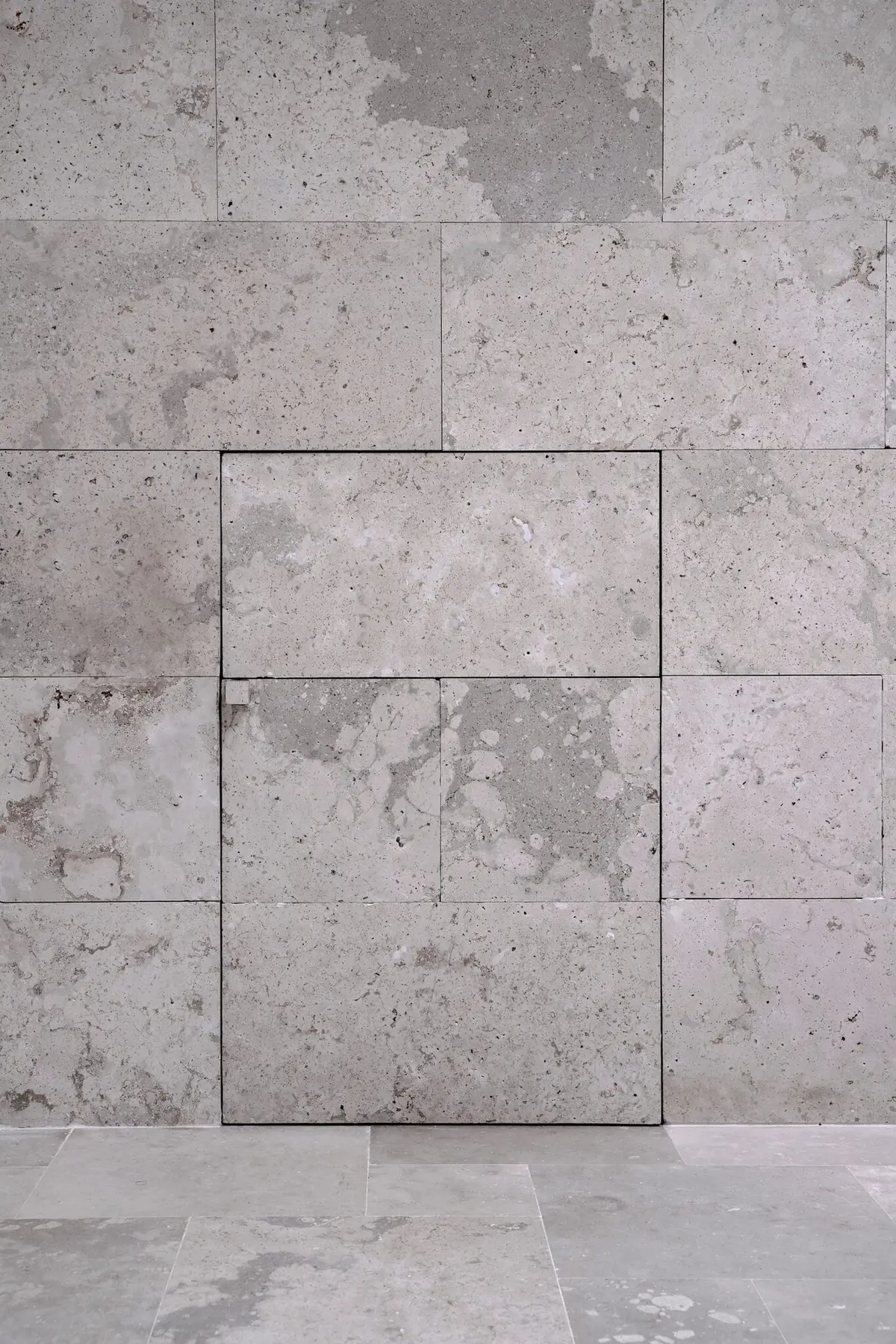 Wall clad in grey limestone pieces with cavities and a door set flush within the same cladding