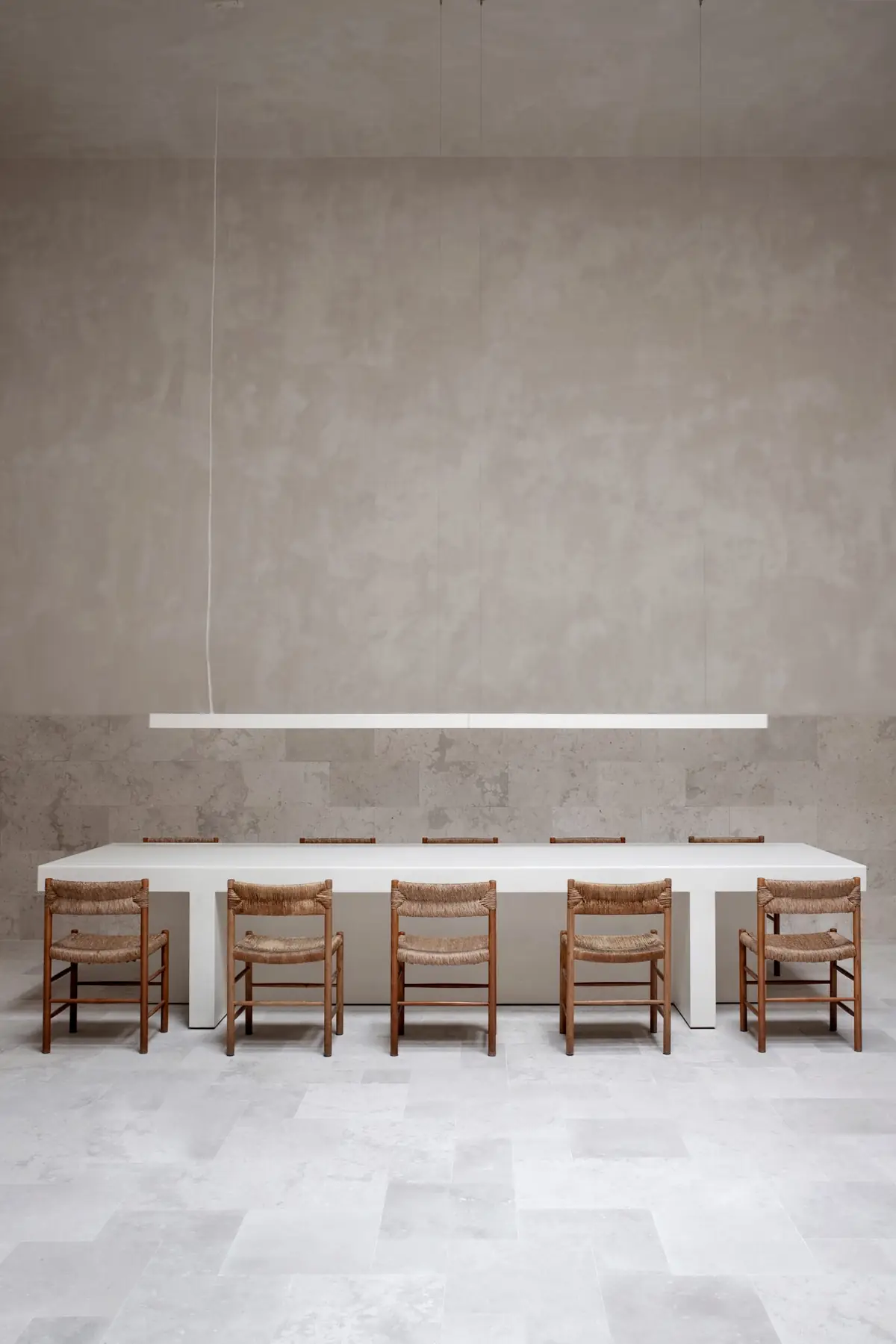 Long white meeting table with ten wooden chairs with rush seats beneath a linear light fitting