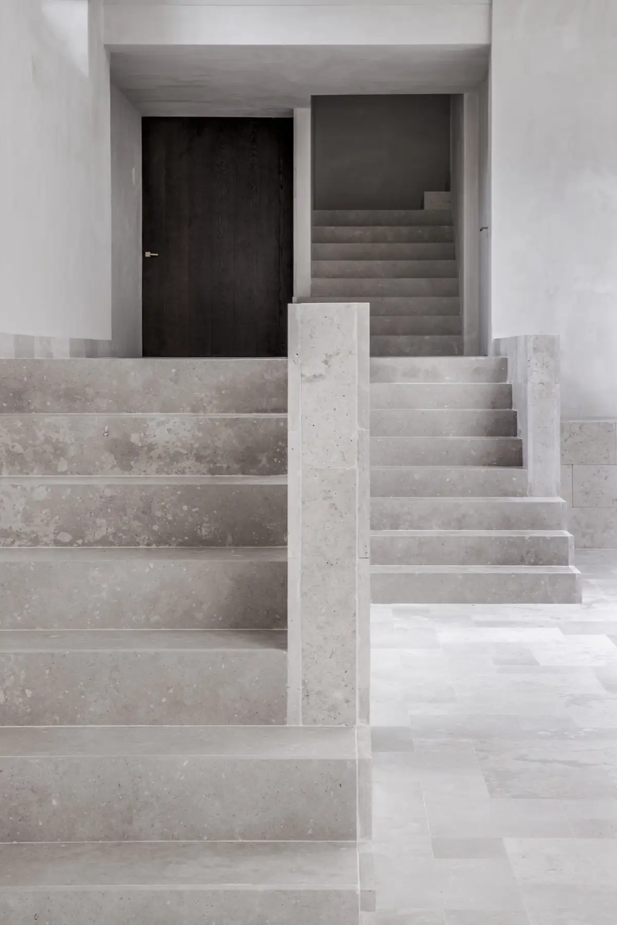 Staircase clad in pale limestone rising towards a dark wooden door