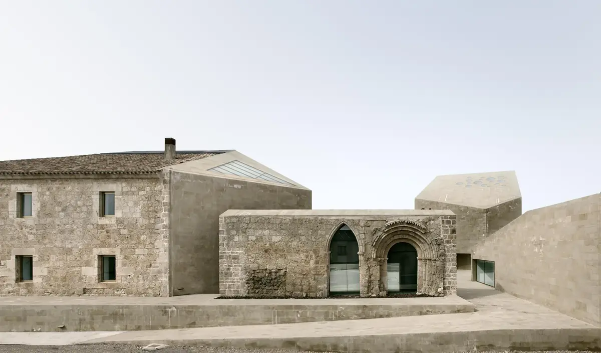 Former stone hospital beside a volume incorporating a pointed arch and a Romanesque portal