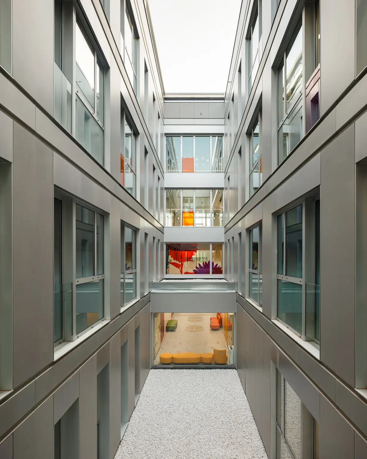 Patio interior con fachadas de paneles grises y ventanales hacia una sala de juegos