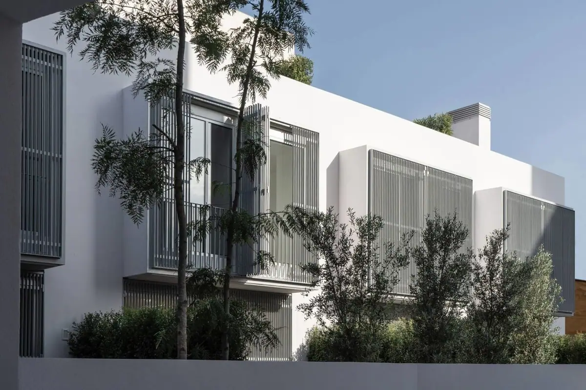 White inner facade with grey metal screens and trees in front