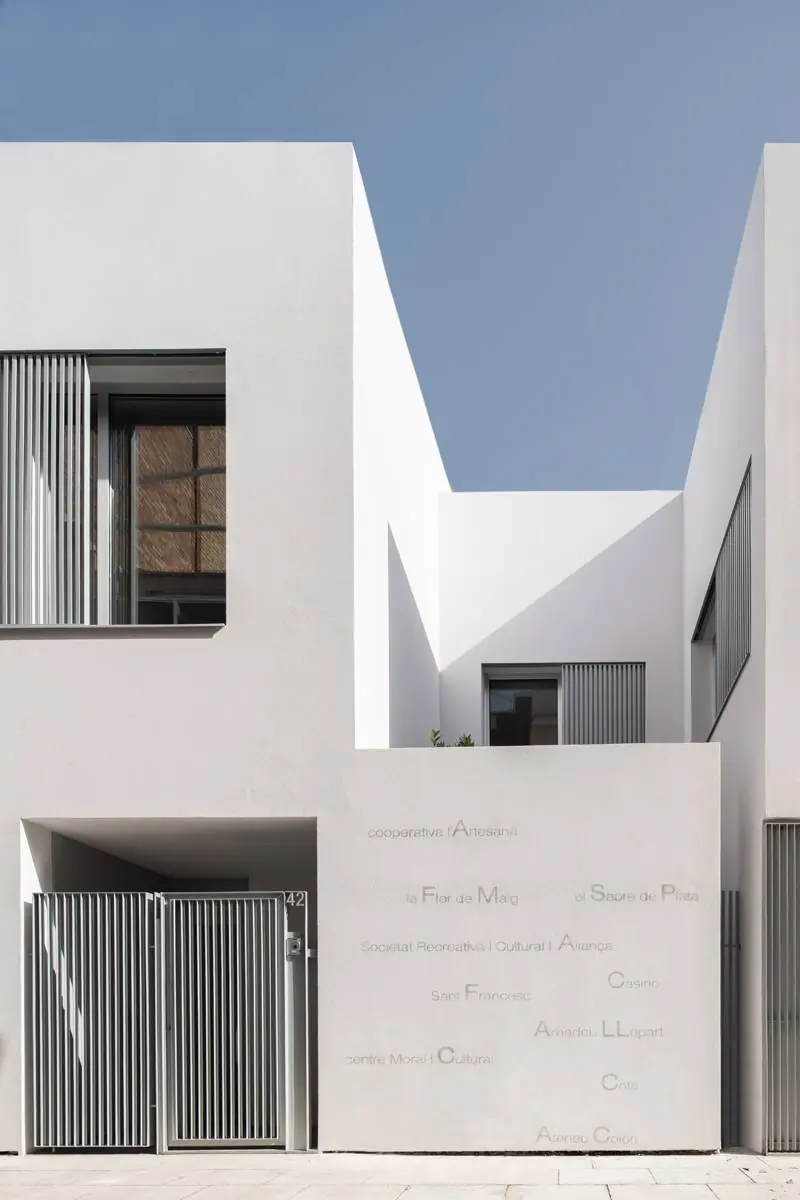 White ground-floor wall with neighbourhood names painted in grey beside a slatted door