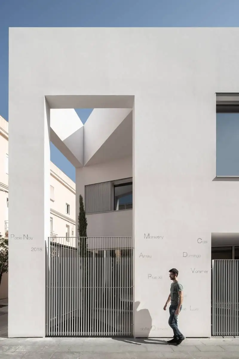 Large opening in the white facade with a cypress and a slatted door, and a pedestrian in front
