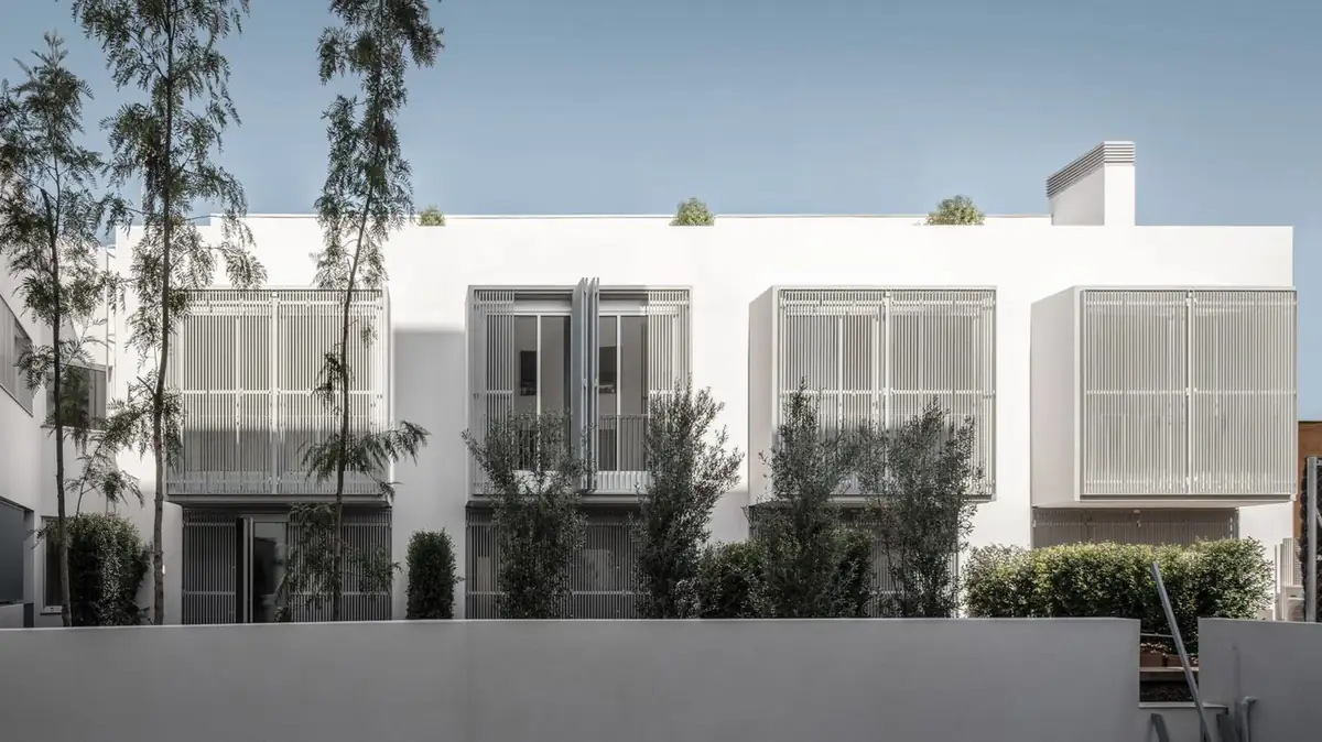 White facade of the houses with four bays of screens and trees in the foreground