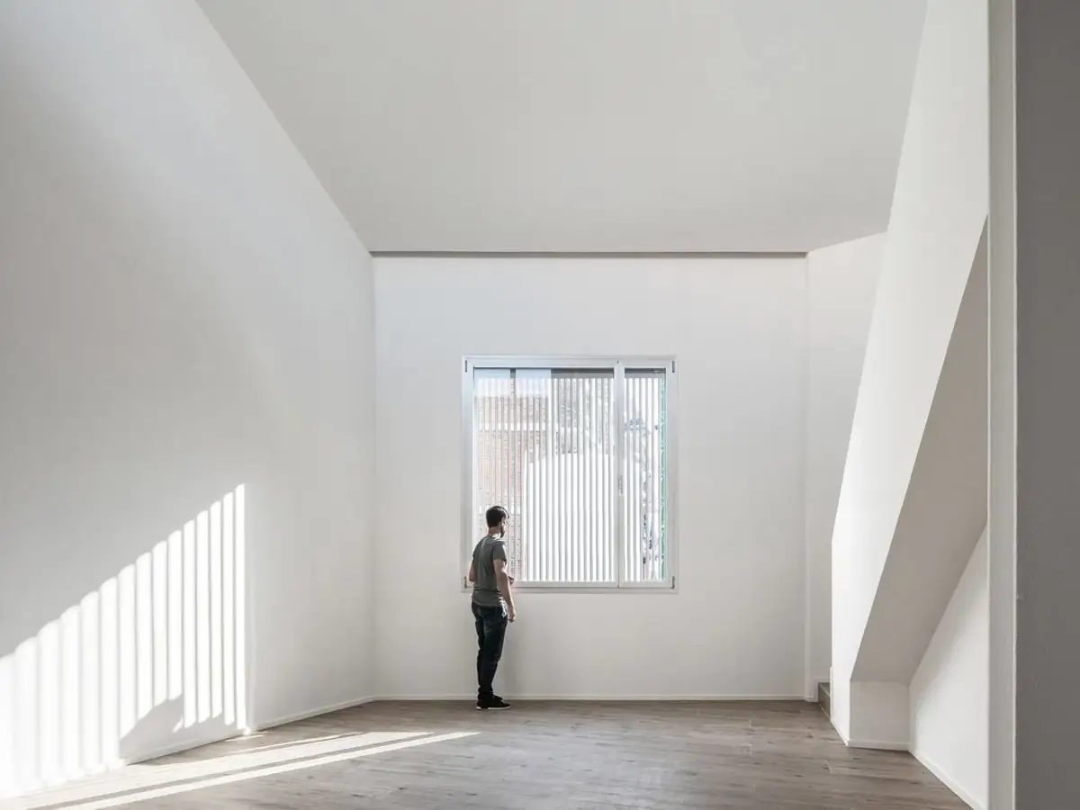 Double-height bedroom with white walls, a slatted window and striped light on the wall