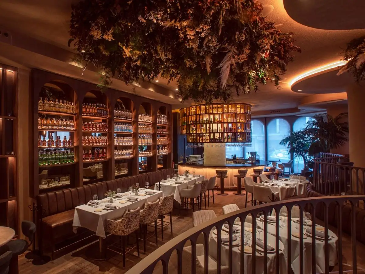 Comedor de La Única con mesas vestidas, botellería en hornacinas de arco, barra circular retroiluminada y vegetación colgada del techo