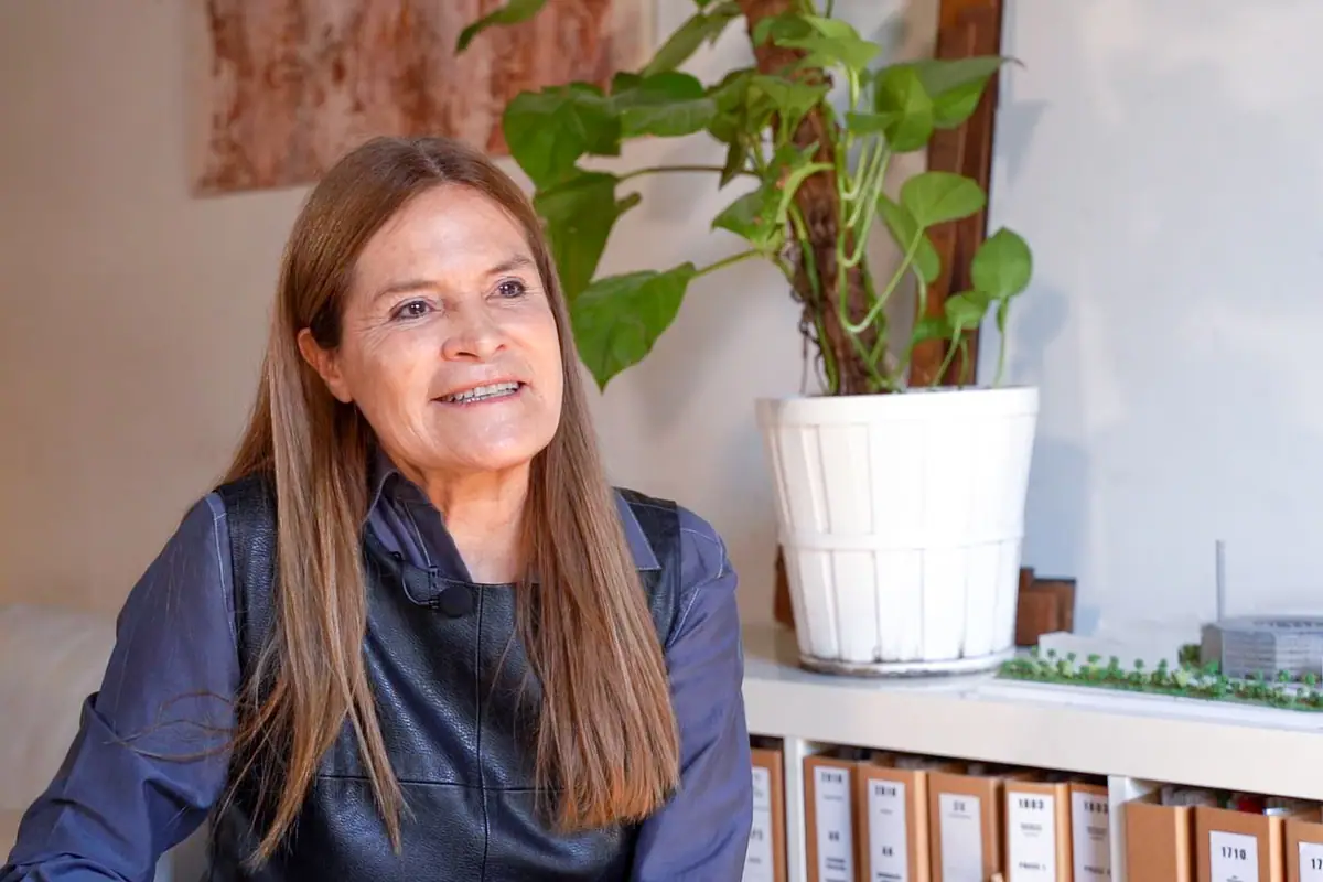 Retrato de Carmen Santana durante la entrevista, sonriente, junto a una planta y archivadores del estudio