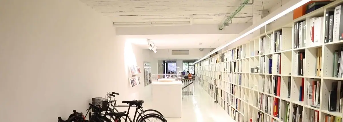A white corridor in the studio with a long shelf of magazines and files on the right and bicycles parked on the left