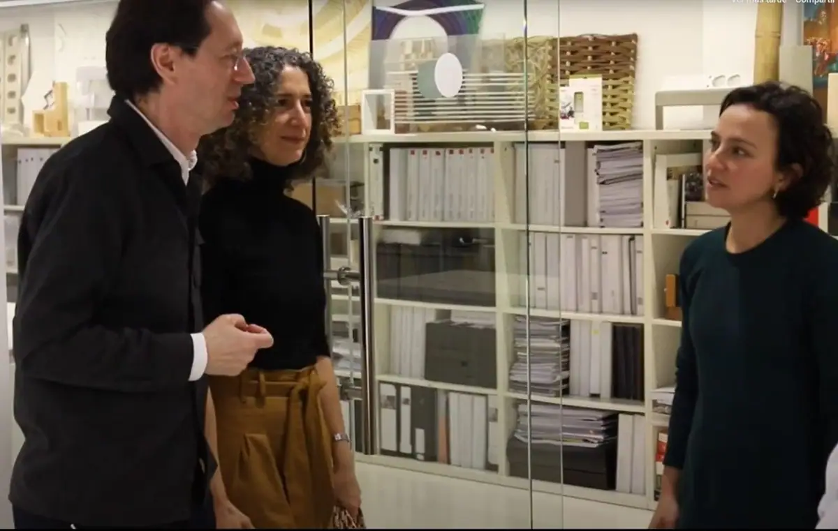 Fermín Vázquez and Ana Bassat talk, standing, with an interviewer in front of shelving with models and files