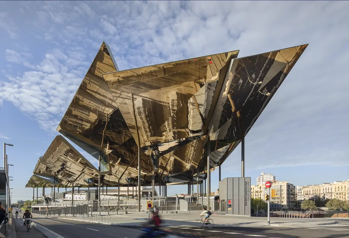 The large roof of gold reflective metal panels of the Mercat dels Encants above the street, with cyclists and apartment buildings in the background