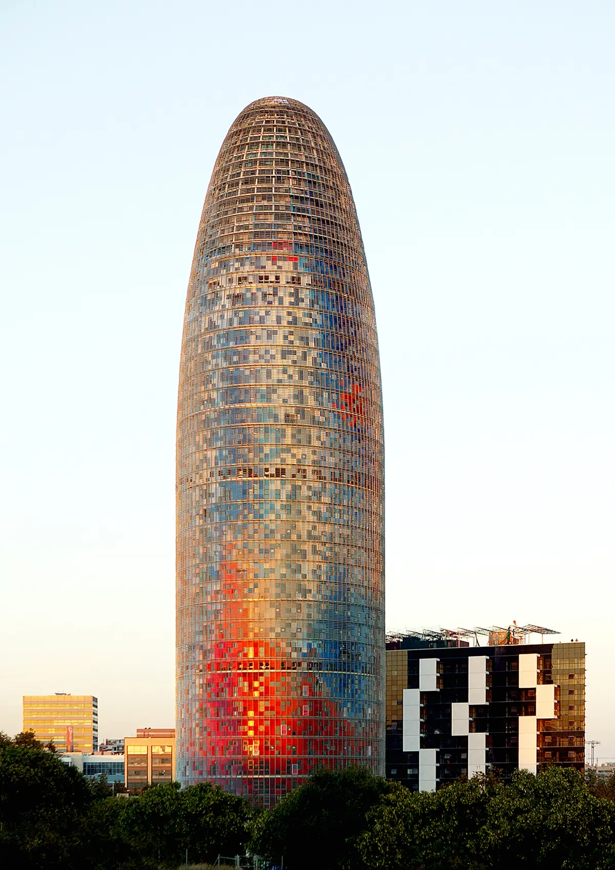Torre Agbar at dusk, with its façade of red and blue louvres above the greenery