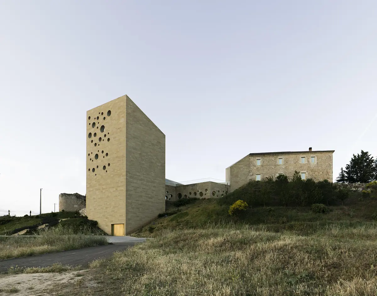 Torre de piedra con perforaciones circulares junto a un antiguo edificio de piedra en lo alto de una ladera