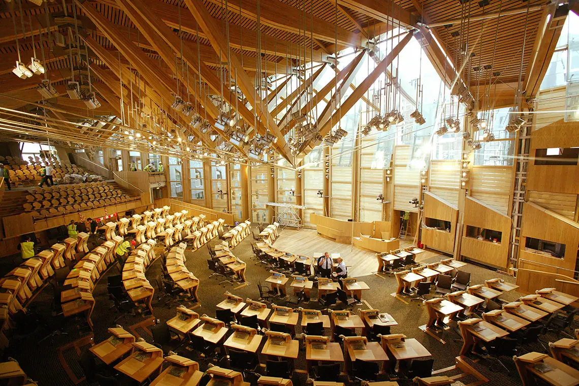 The debating chamber of the Scottish Parliament, with seating in a semicircle and a roof of timber beams