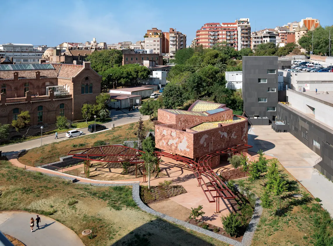 Kálida Sant Pau Centre, a brick volume with ceramic lattices and red pergolas, with the Modernista pavilions of Sant Pau in the background