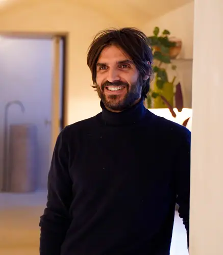 Portrait of Xabier Ortega smiling, wearing a black polo-neck jumper, in a pale interior