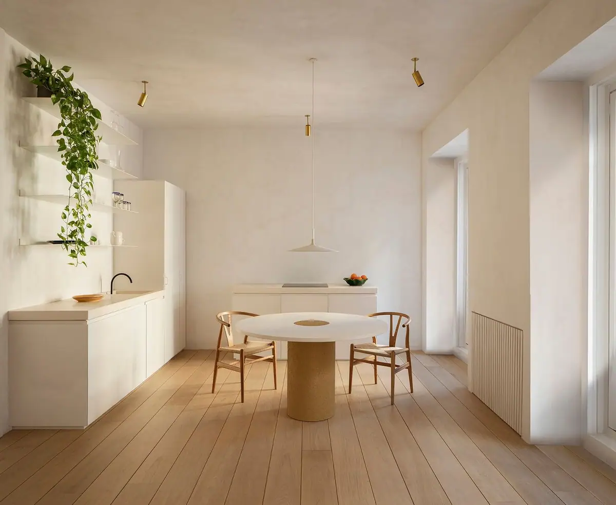 White-walled open kitchen with a round table, two wooden chairs and a wide-plank oak floor