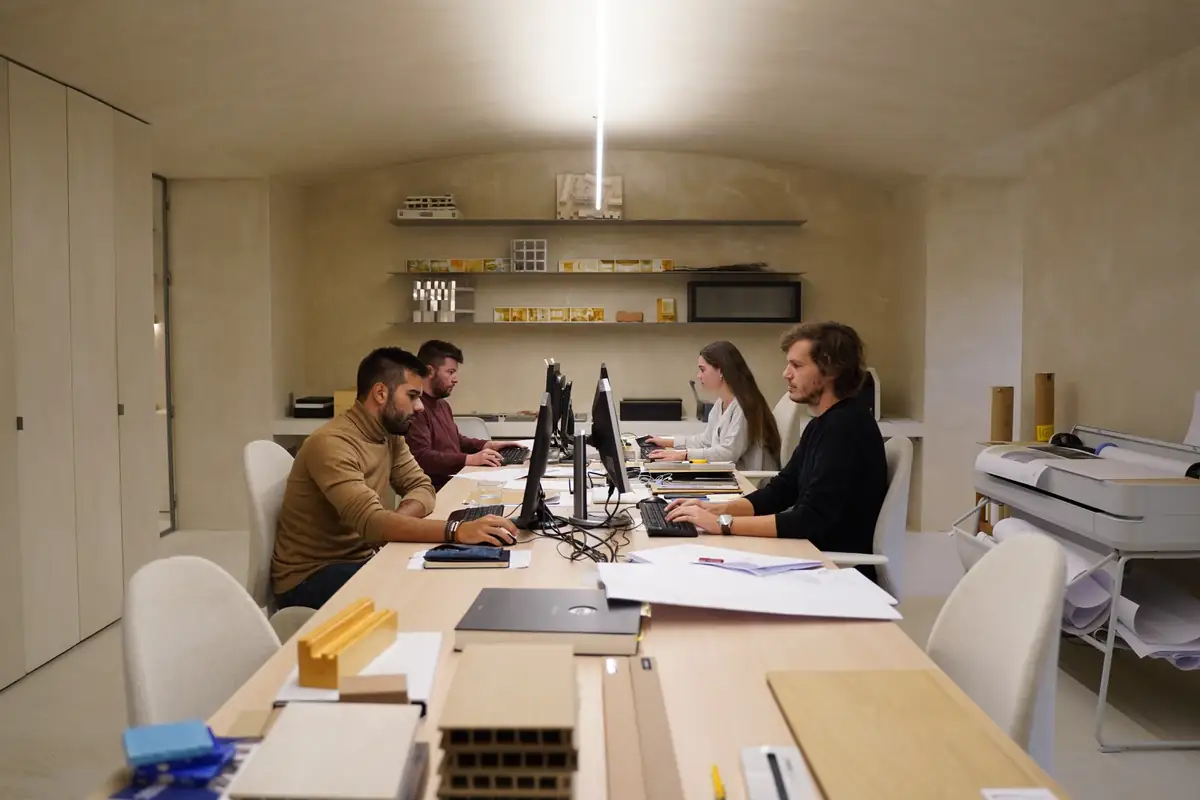 Team working at a long table in the BETA.Ø office, with material samples and models in the foreground