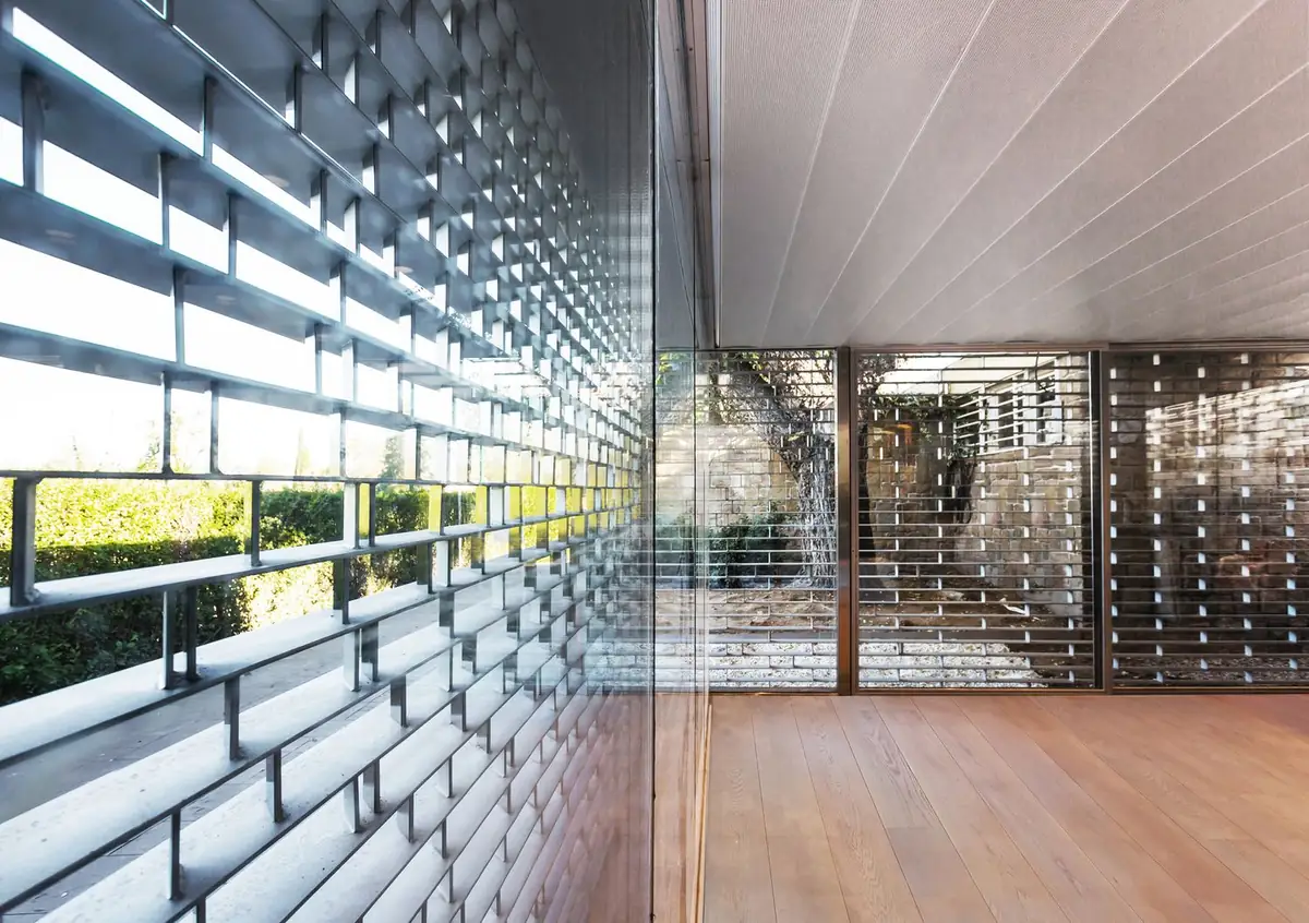 External screen of horizontal slats behind a glass enclosure, with a wooden floor and a courtyard beyond