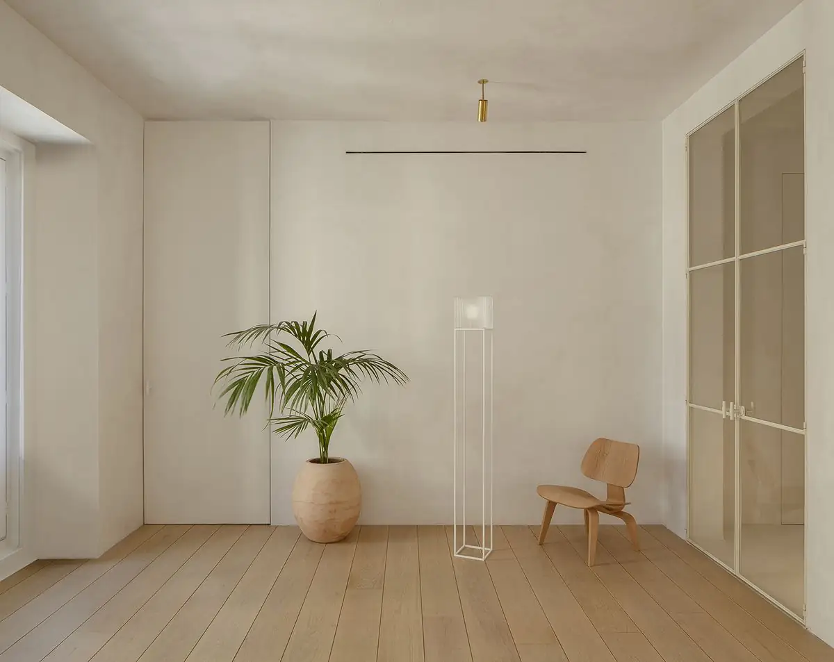 Pale-walled room with an oak floor, a palm in a terracotta pot, a floor lamp and a glazed door