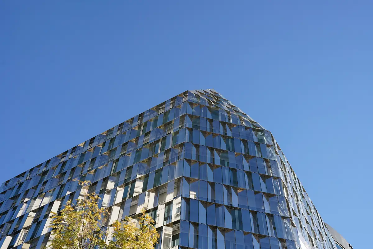 Corner of the office building at Paseo de la Castellana 94 with its faceted glass façade against a blue sky