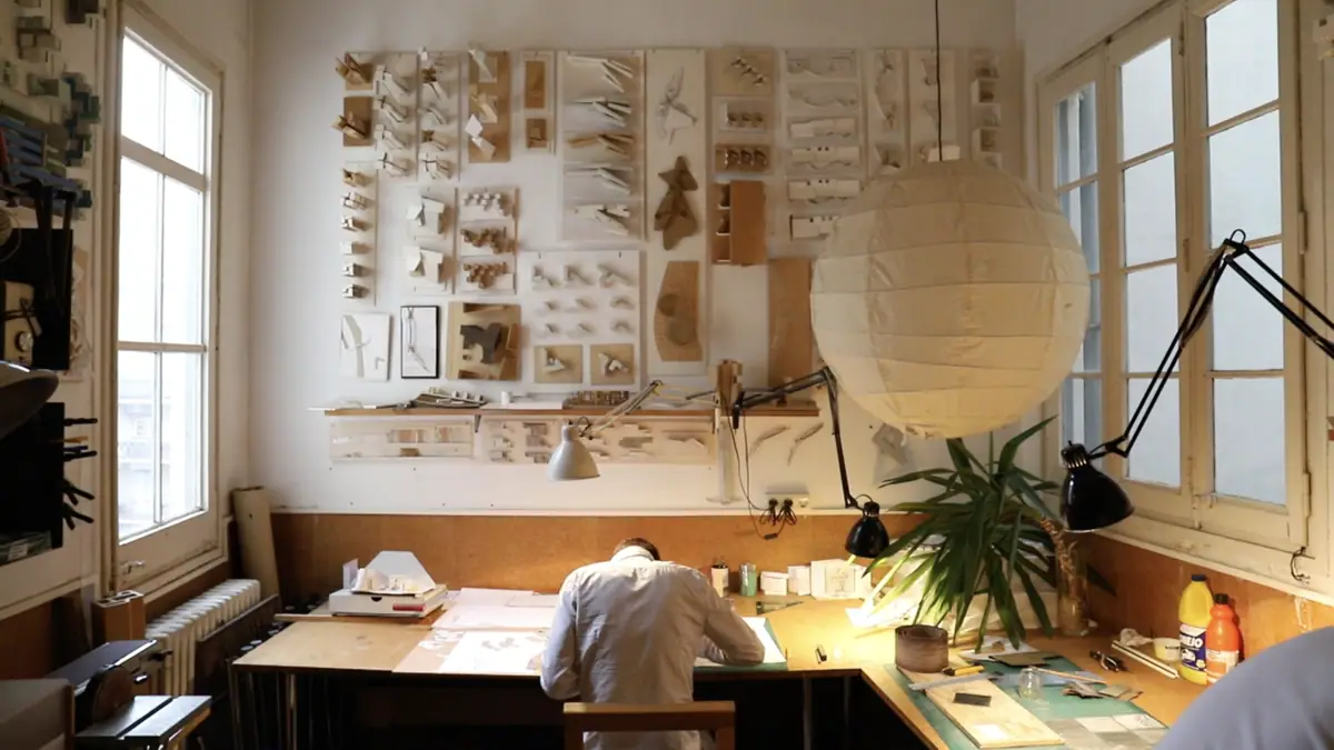 Architect drawing at a desk beneath a wall full of study models