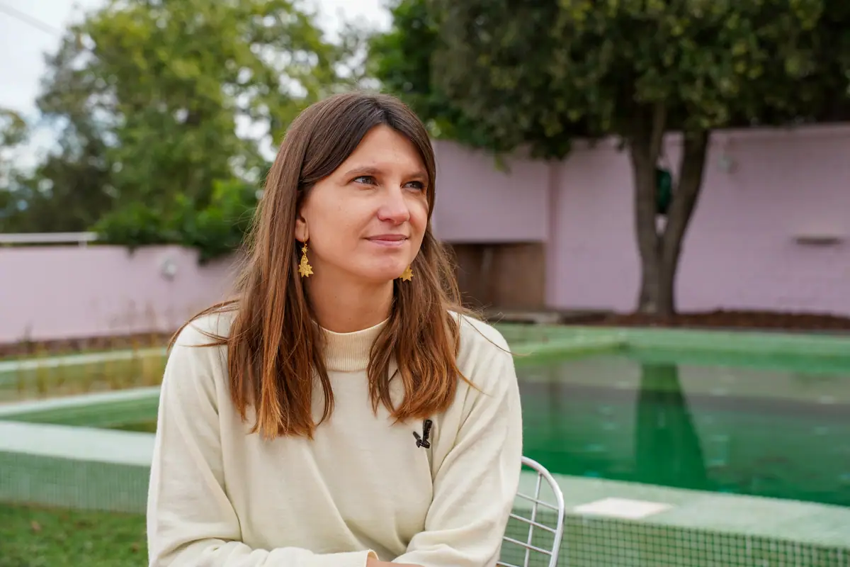 Clara Vidal, con jersey claro, sentada junto a una piscina con un muro rosa al fondo
