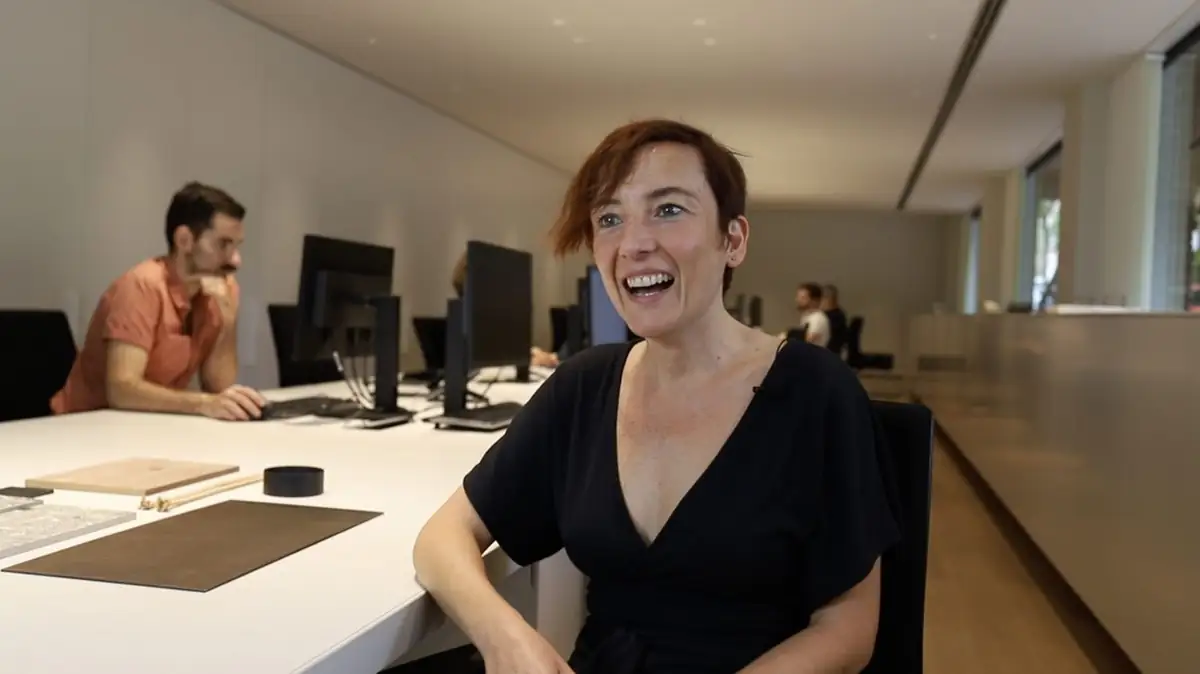 A team member smiles during filming, seated at a long table with material samples