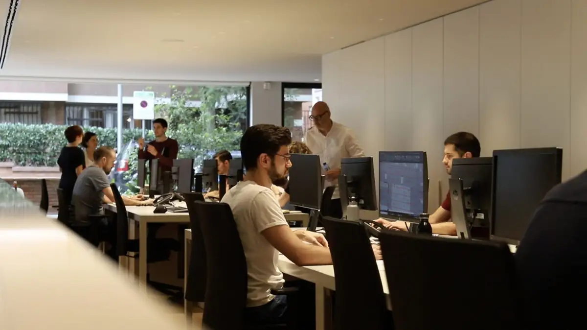 Francesc Rifé, standing in a white shirt, talks with the team in the workroom