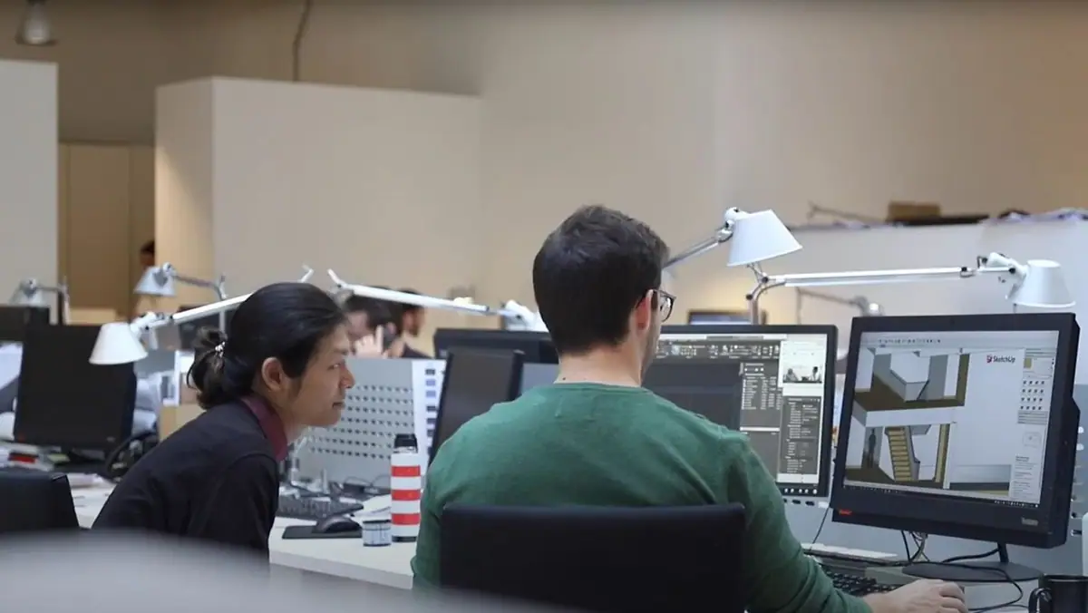 Dos arquitectos trabajan ante un monitor con un modelo 3D en una oficina diáfana con flexos blancos