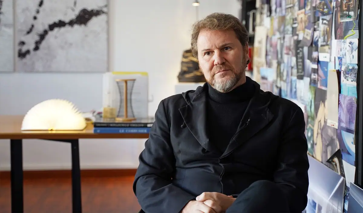 Diego Gronda, bearded and in a black roll-neck jumper, seated in his studio in front of a board of reference images