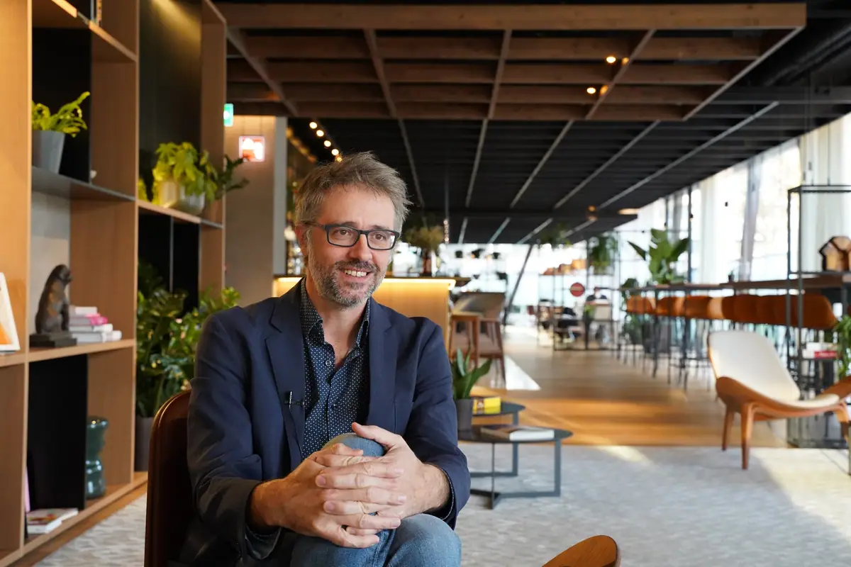 Ferran Tortosa, in glasses and a blue jacket, seated in a lounge area with a wooden grid ceiling