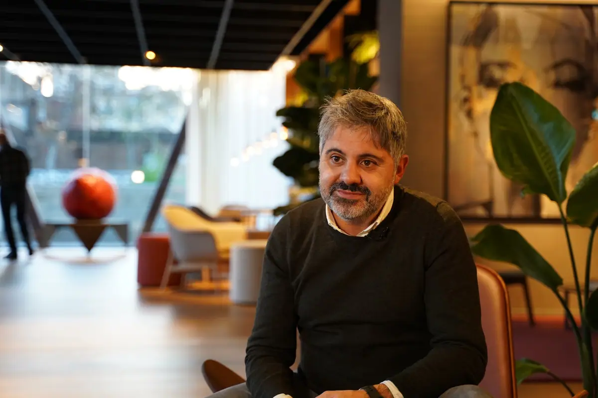 Ernest Boronat, in a dark jumper, during the interview in a lounge area with plants and a large red sphere in the background