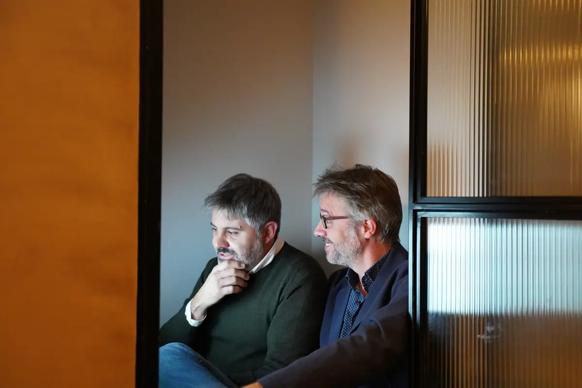 Ernest Boronat and Ferran Tortosa seated together behind a fluted glass door, looking to one side