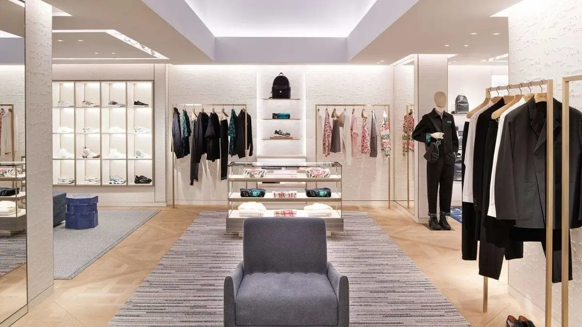 Interior of the Dior store in Oslo, with clothes rails, illuminated shelving, a grey armchair and striped rugs