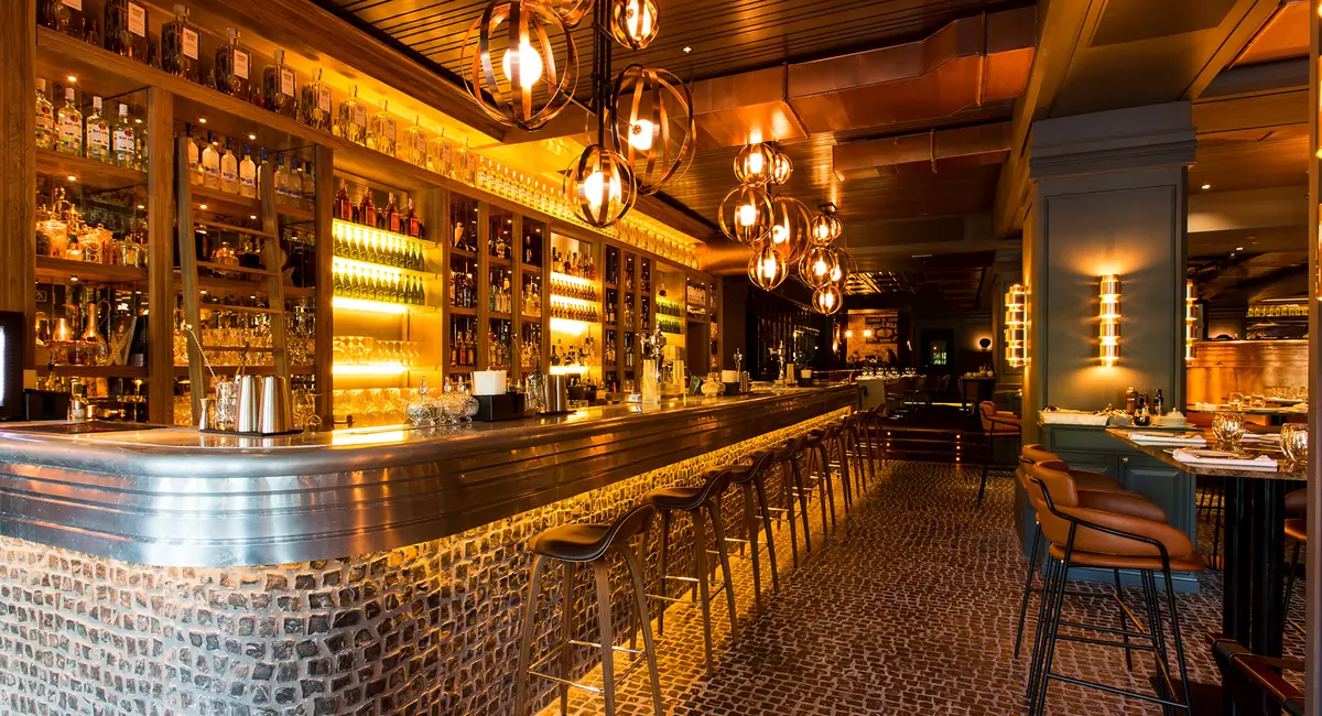 Bar of the Tatel Madrid restaurant with a stone front, metal top, illuminated bottle racks and spherical brass lamps
