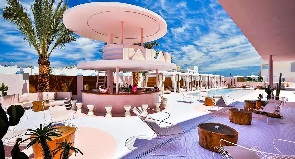 Pool terrace of the Paradiso Ibiza Art Hotel with a pink circular bar, palm trees, cacti and white sun loungers