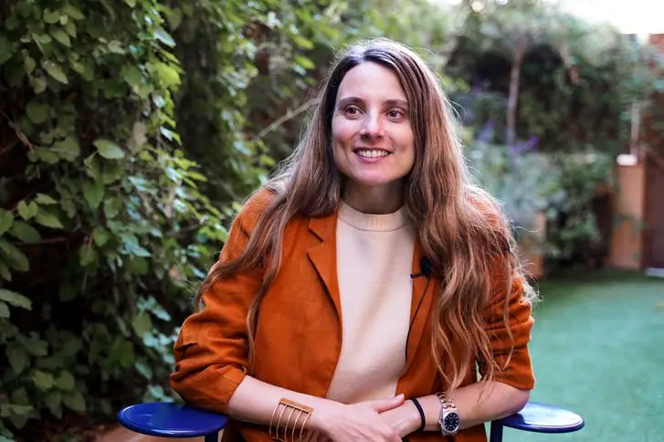 Portrait of Cristina Domínguez Lucas, in an orange jacket, smiling in a garden