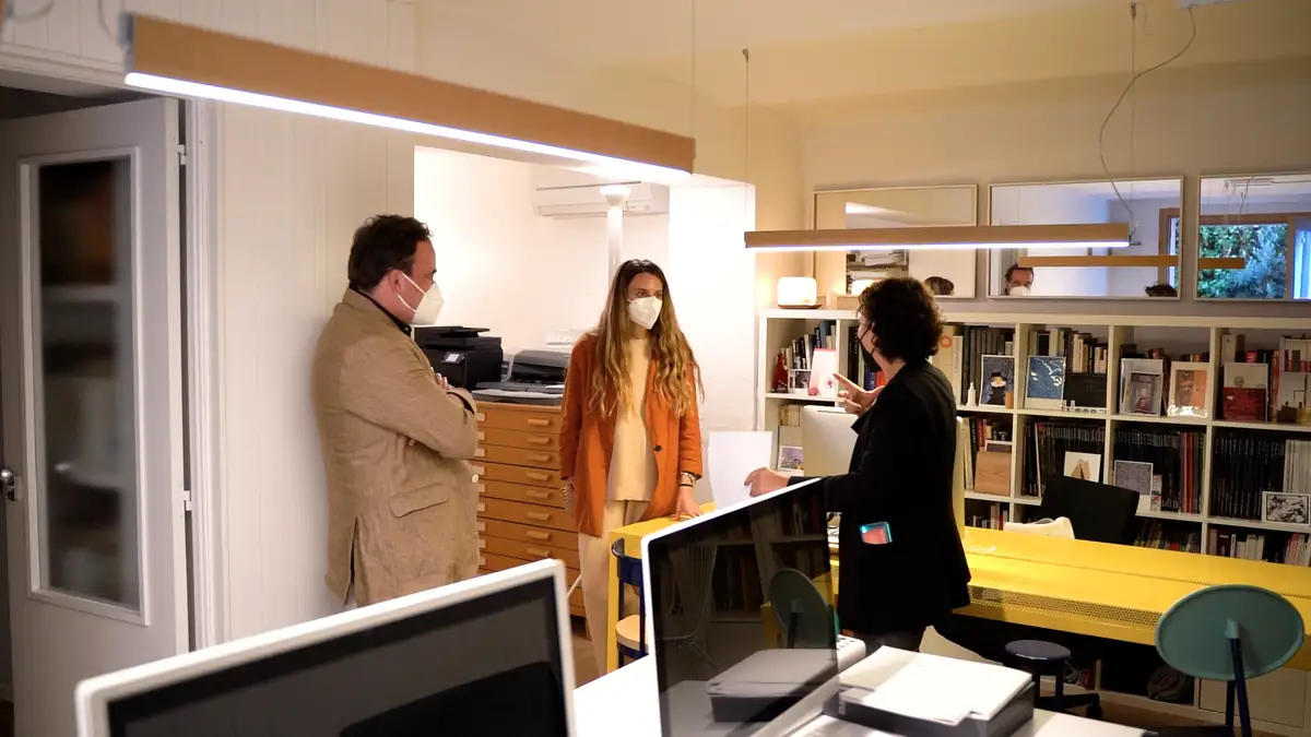 The two architects talking, standing in an office with bookshelves and a yellow table