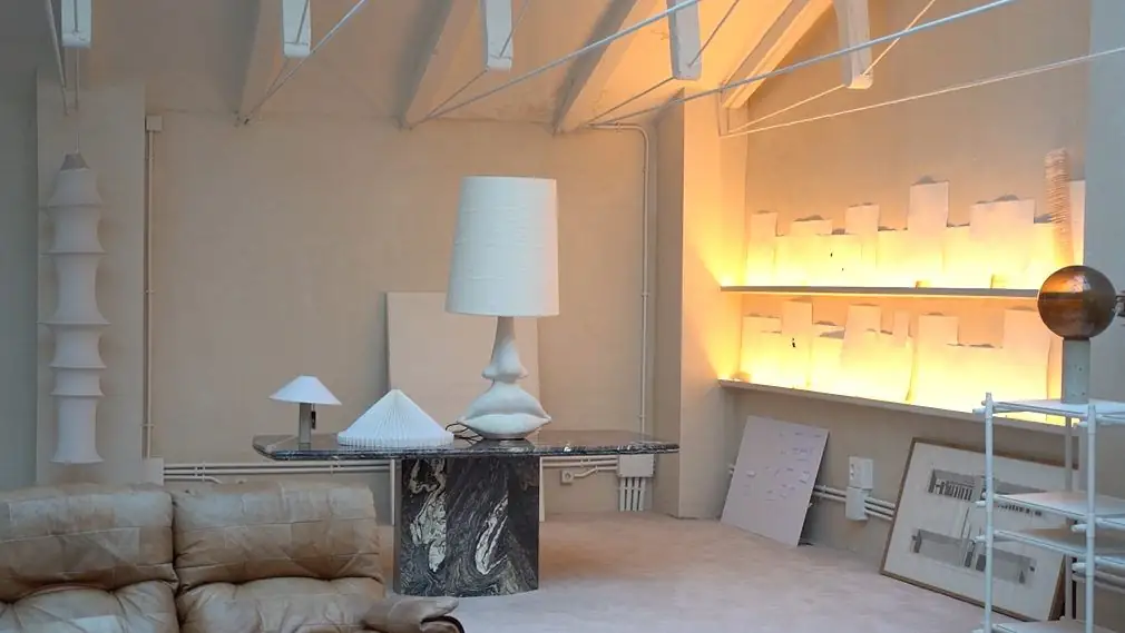 Rincón con lámpara blanca de pie, mesa de mármol oscuro y baldas iluminadas con láminas de papel